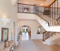 Grand entrance foyer with coral stone walls, high ceilings, and a stunning wrought iron staircase at Benjoli Breeze, a luxury villa in Barbados.