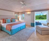 Master bedroom at Coconut Grove 2 with a king-size bed, vibrant tropical decor, en-suite bathroom, and private balcony overlooking the golf course.