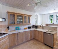 Fully equipped modern kitchen at Coconut Grove 2, Royal Westmoreland, featuring custom wood cabinetry, stainless steel appliances, and breakfast bar.