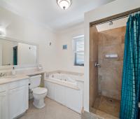 Bright Master bathroom featuring a walk-in shower with natural stone tiles, spacious tub, large vanity, and window at Blue Waters 1 vacation rental Barbados.