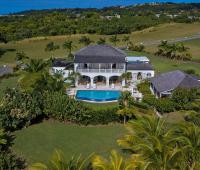 A breathtaking aerial view of Howzat Villa in Royal Westmoreland, Barbados, showcasing its luxurious architecture, lush gardens, and golf course surroundings.