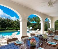 Elegant covered patio at Howzat Villa, Barbados, featuring outdoor dining, lounge seating, and serene golf course views for a perfect Caribbean retreat.