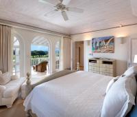 A bright and airy guest bedroom at Howzat Villa, Barbados, with twin beds, stylish decor, and a private patio with lush tropical views.
