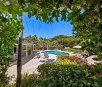 View from the dining area to the pool deck, showcasing outdoor seating and lush tropical landscaping at Ixora Royal Westmoreland, Barbados