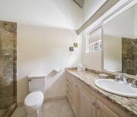 Elegant guest bathroom at Sandalwood House, featuring a granite countertop, glass-enclosed shower with stone tiles, and a large mirror