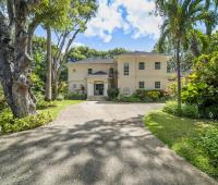 Grand entrance to Sandalwood House, surrounded by lush tropical gardens and mature trees, with a spacious driveway.