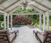 Relaxing covered patio at Sandalwood House Guest Cottage, complete with cushioned loungers and offering views of the landscaped garden and jacuzzi