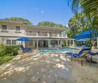 Outdoor pool area at Sandalwood House, complete with lounge chairs, umbrellas, and lush garden surrounding