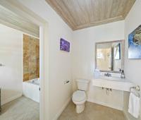 Full guest bathroom at Sandalwood House featuring natural wood ceiling, stone-tiled walls, and a soaking tub