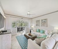 Bright and inviting living room in Seabreeze Penthouse, Sugar Hill Resort, Barbados, with elegant coastal decor, comfortable white sofas accented by turquoise cushions, and large glass doors opening to a spacious balcony overlooking tropical greenery.