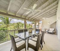 Dining area on the balcony of Seabreeze Penthouse, Sugar Hill Resort, Barbados, with a glass-top table and wicker chairs, surrounded by tropical palm trees, making it an ideal spot for al fresco dining in a tranquil setting.