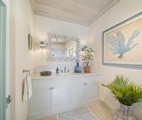 Image of the vanity area in the bathroom at Seascape, Barbados: A luxurious bathroom vanity adorned with a shell-themed mirror, modern fixtures, and vibrant green plants, creating a relaxing and inviting ambiance ideal for guests at this Barbados rental villa.