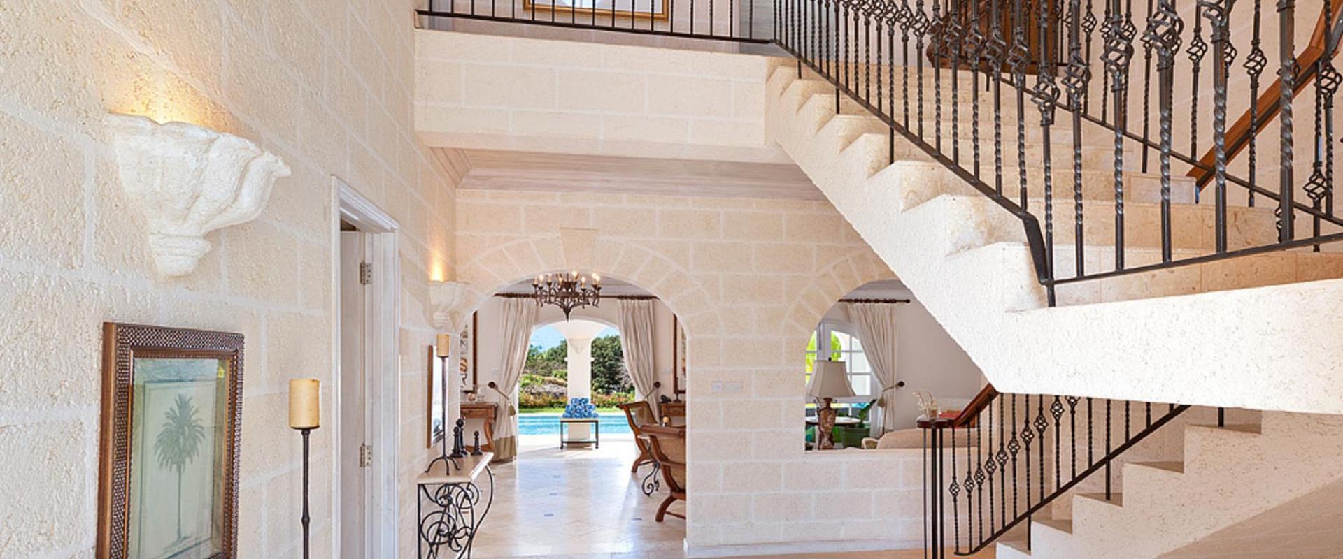 Grand entrance foyer with coral stone walls, high ceilings, and a stunning wrought iron staircase at Benjoli Breeze, a luxury villa in Barbados.