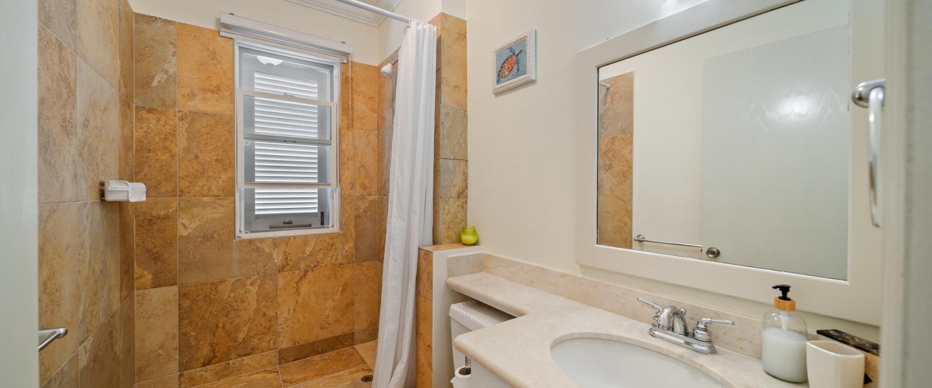 Bright Shared bathroom featuring a walk-in shower with natural stone tiles, large vanity, and window at Blue Waters 1 vacation rental Barbados.
