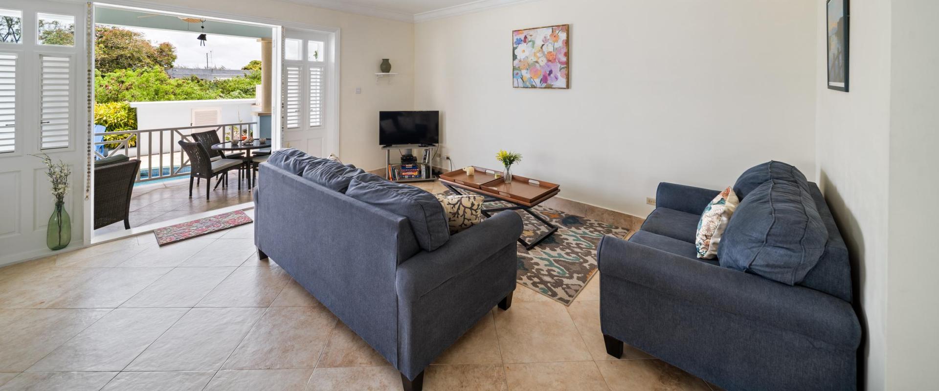 Bright and spacious living room with comfortable sofas, TV, and open plan access to the patio and private pool at Blue Waters 1 vacation home Barbados.
