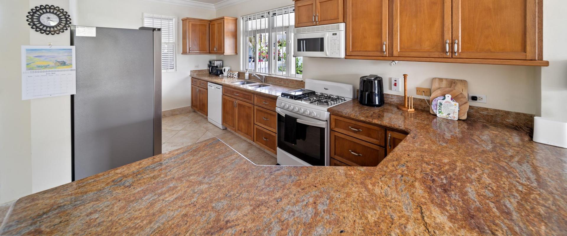 Bright kitchen at Blue Waters 1 featuring wood cabinetry, modern appliances, and garden views perfect for a self-catered Barbados holiday.