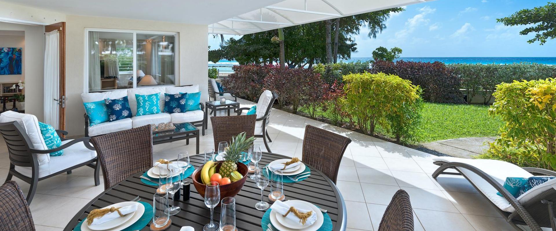 A spacious covered patio at Palm Beach 101 in Barbados, featuring an outdoor dining table, lounge seating, and breathtaking ocean views.