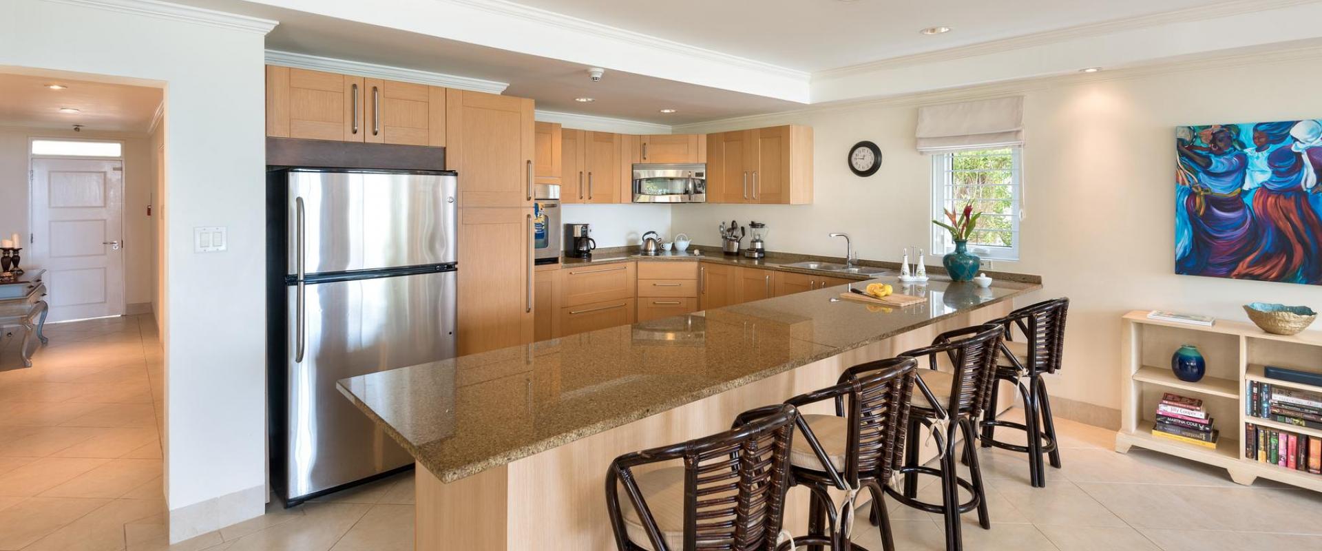 A sleek, fully equipped kitchen with stainless steel appliances, granite countertops, and a breakfast bar with elegant high stools at Palm Beach 101.