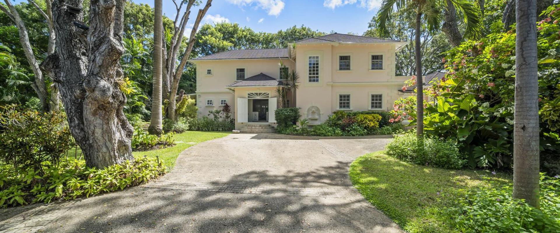 Grand entrance to Sandalwood House, surrounded by lush tropical gardens and mature trees, with a spacious driveway.