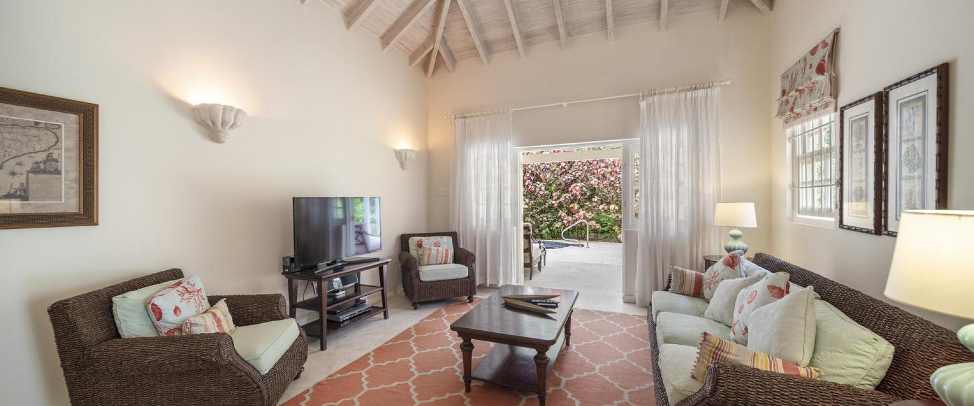 Guest Cottage living room at Sandalwood House, with high vaulted ceilings, wicker furnishings, and views of the garden through wide doors.