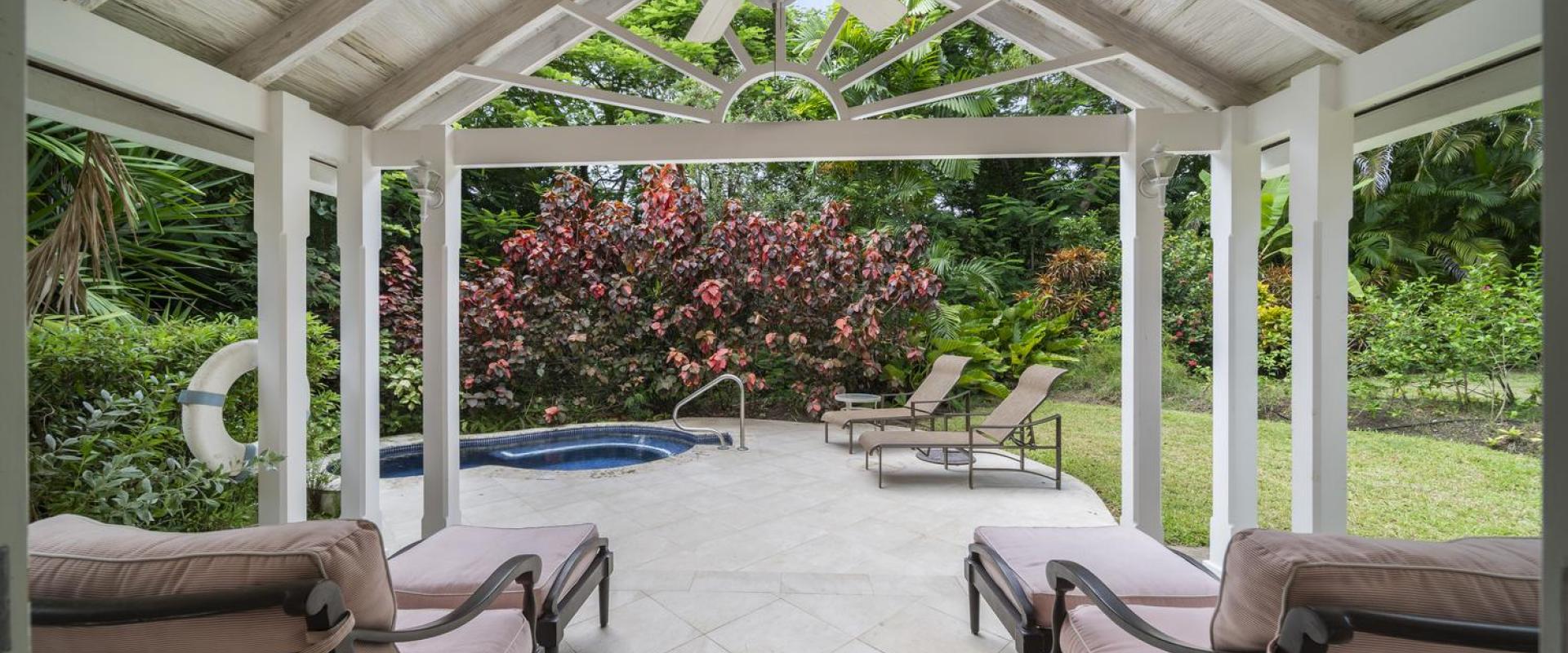 Relaxing covered patio at Sandalwood House Guest Cottage, complete with cushioned loungers and offering views of the landscaped garden and jacuzzi