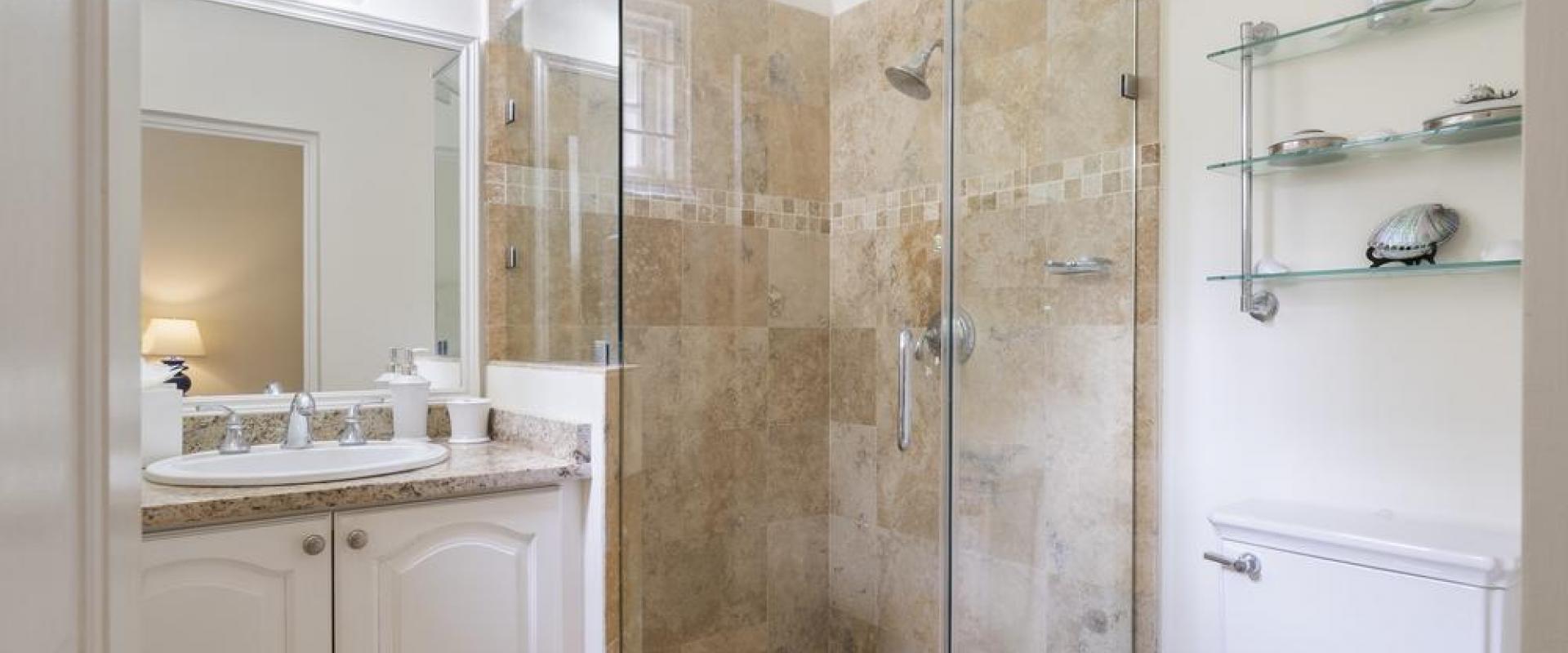 Cottage bathroom one at Sandalwood House with a glass-enclosed shower, neutral stone tiles, and a bright, airy design