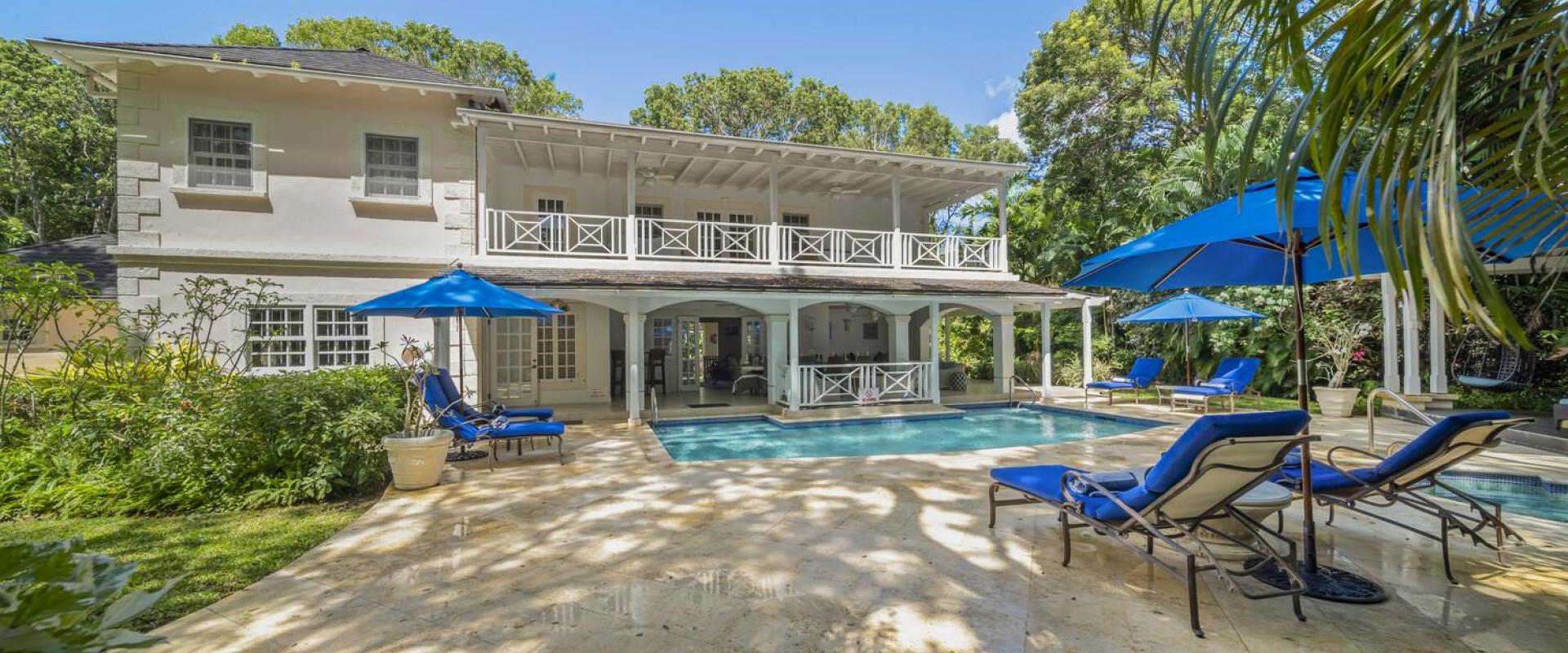 Outdoor pool area at Sandalwood House, complete with lounge chairs, umbrellas, and lush garden surrounding