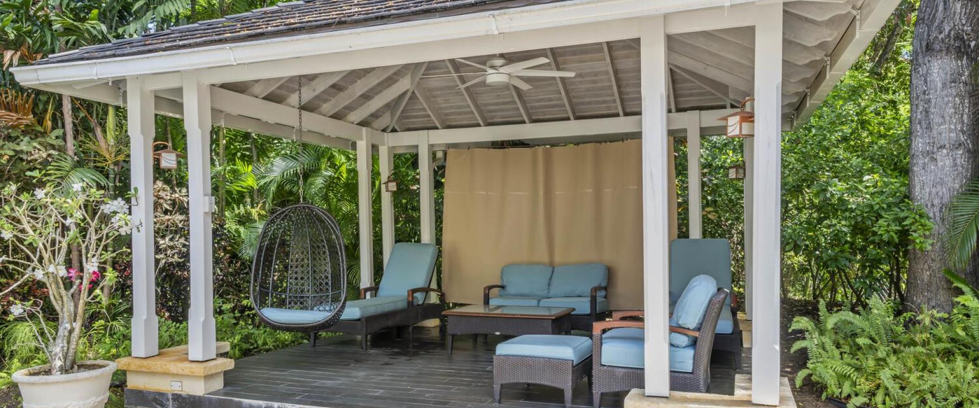 Poolside cabana at Sandalwood House offering a shaded seating area, ceiling fan, and lush garden views