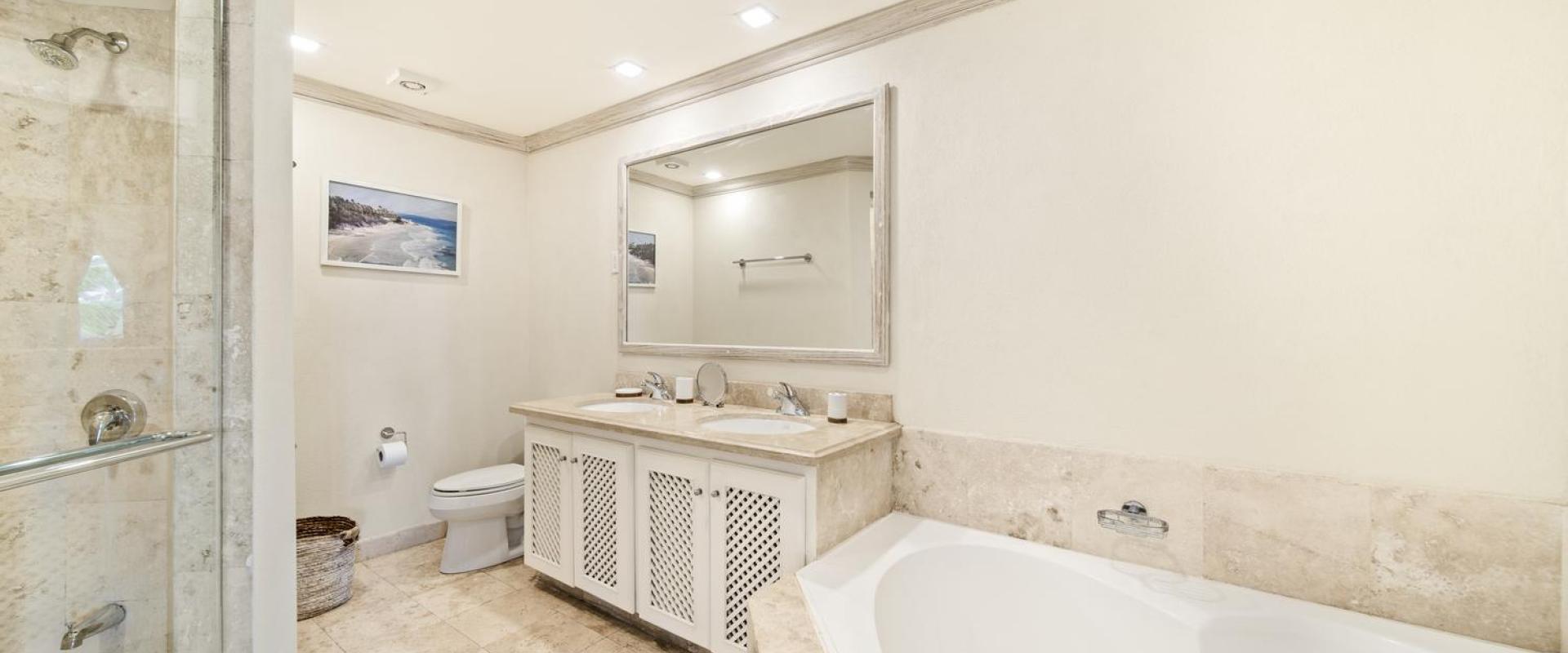 Modern bathroom in Seabreeze Penthouse, Sugar Hill Resort, Barbados, featuring dual sinks, marble countertops, a spacious shower, and a luxurious bathtub, combining functionality with elegant design.