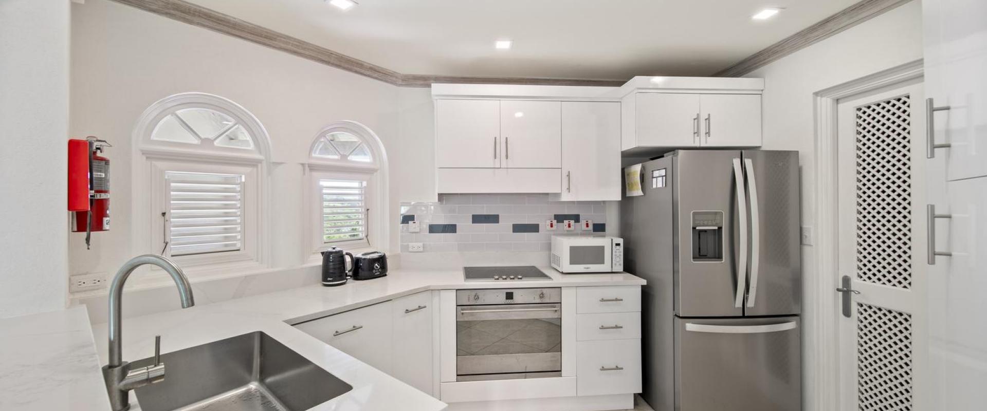 Modern kitchen in Seabreeze Penthouse, Sugar Hill Resort, Barbados, featuring stainless steel appliances, sleek white cabinetry, and a large sink, providing a functional and stylish space for cooking and entertaining.