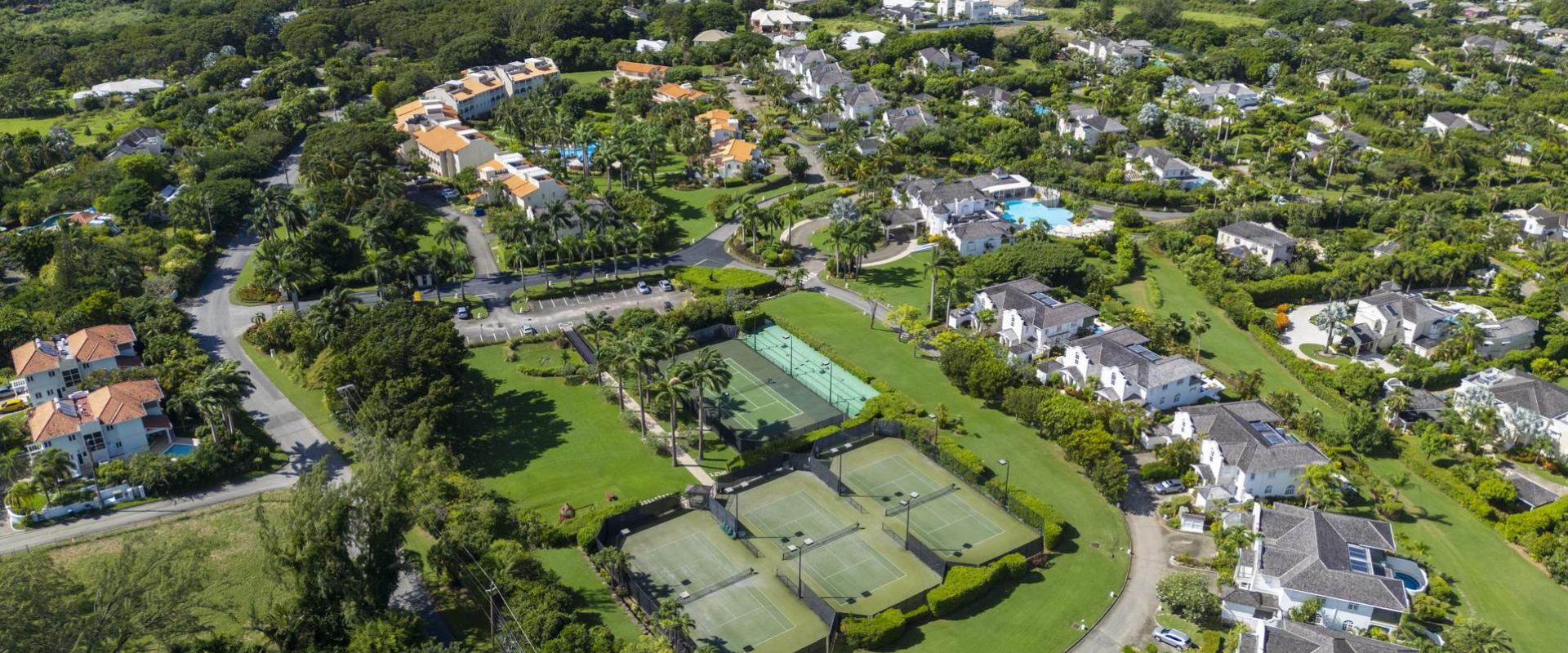 Expansive aerial view over Sugar Hill Resort and surrounding luxury estates in Barbados, with clear views of the resort’s central pool and tennis courts, and the stunning Caribbean Sea in the background.