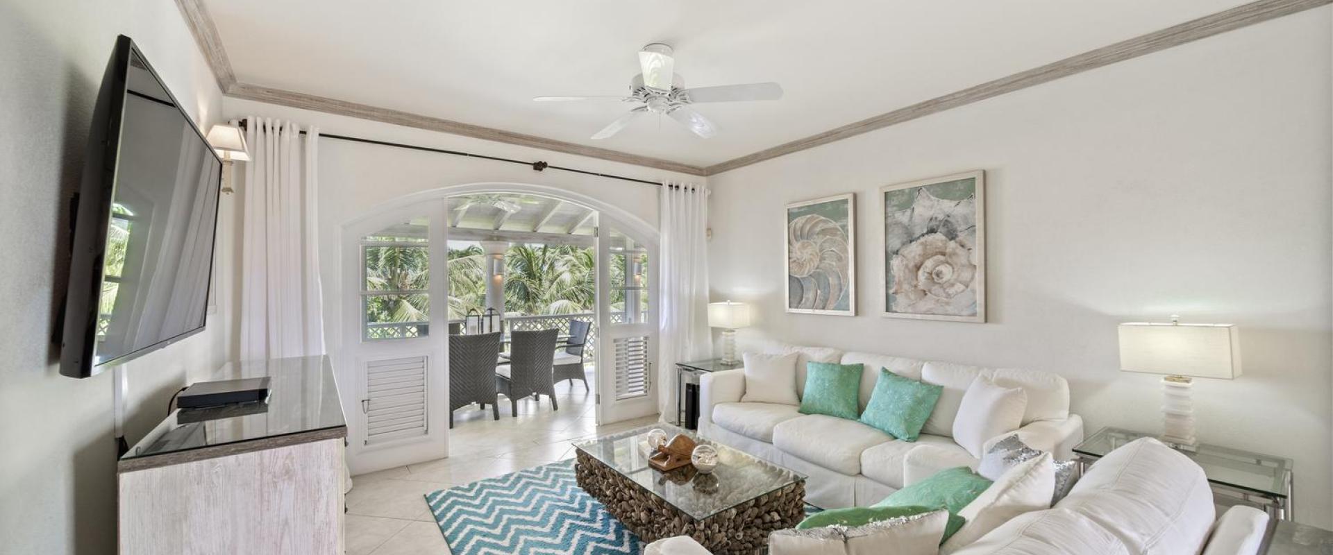 Bright and inviting living room in Seabreeze Penthouse, Sugar Hill Resort, Barbados, with elegant coastal decor, comfortable white sofas accented by turquoise cushions, and large glass doors opening to a spacious balcony overlooking tropical greenery.