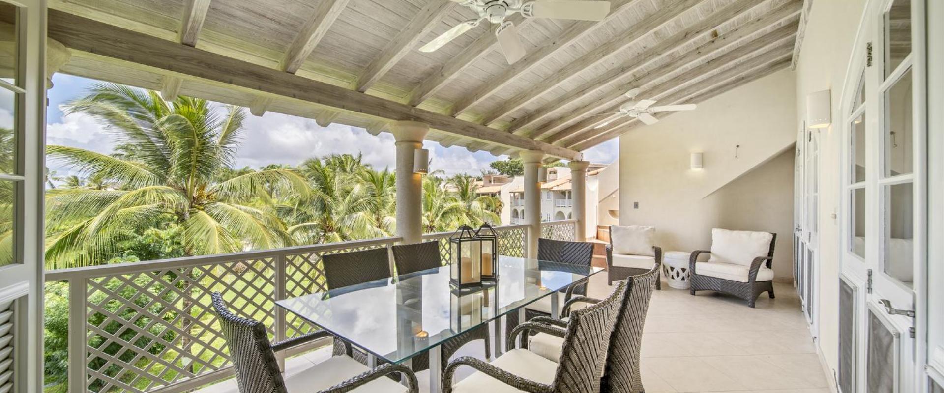 Dining area on the balcony of Seabreeze Penthouse, Sugar Hill Resort, Barbados, with a glass-top table and wicker chairs, surrounded by tropical palm trees, making it an ideal spot for al fresco dining in a tranquil setting.