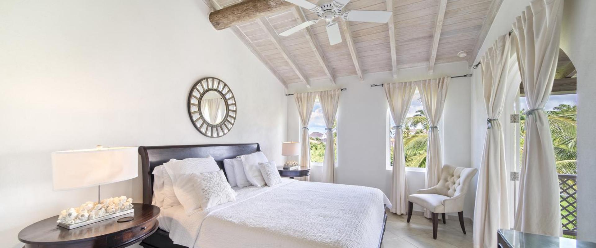 Master bedroom of Seabreeze Penthouse at Sugar Hill Resort, Barbados, with high vaulted ceilings, a plush king-size bed, and large windows that fill the space with natural light, offering a peaceful retreat overlooking the lush resort landscape.