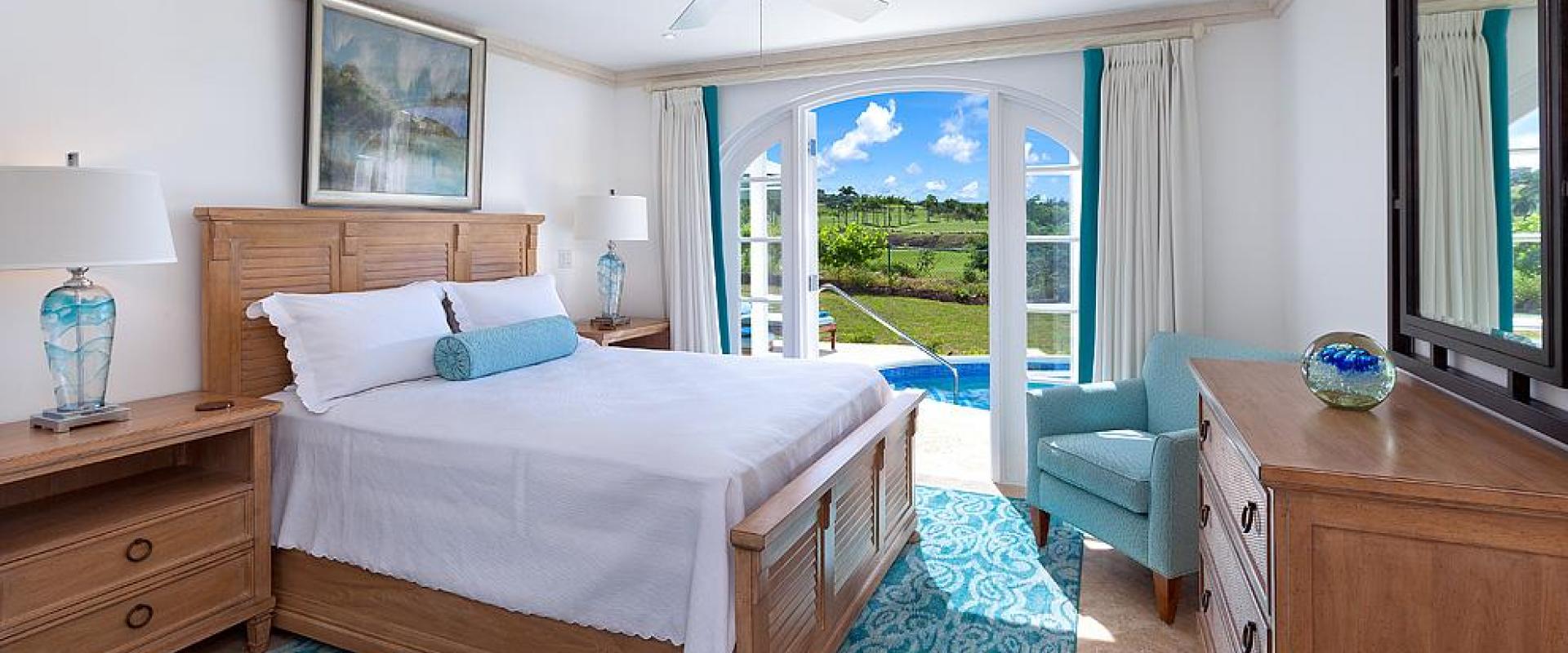 Serene master bedroom with a king-sized bed, pool access, and lush golf course views at Sugar Cane Ridge 22, Royal Westmoreland.