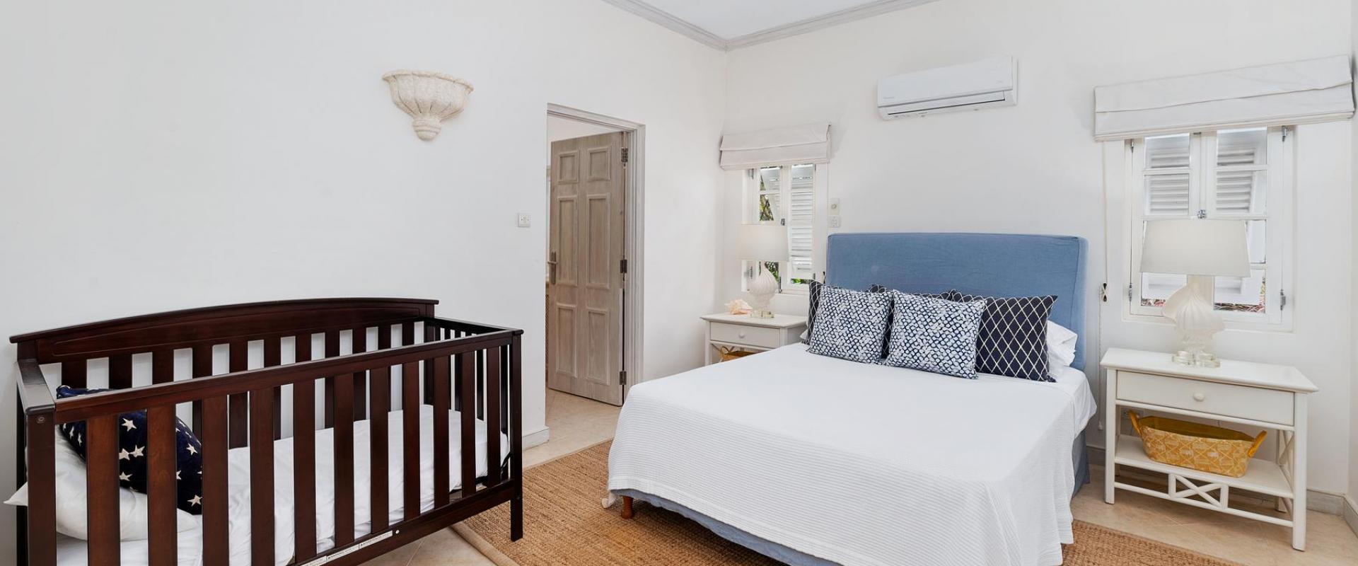 Beautiful bedroom with a plush blue headboard, crisp white linens, and a crib for families at Villa Rosa, Barbados.