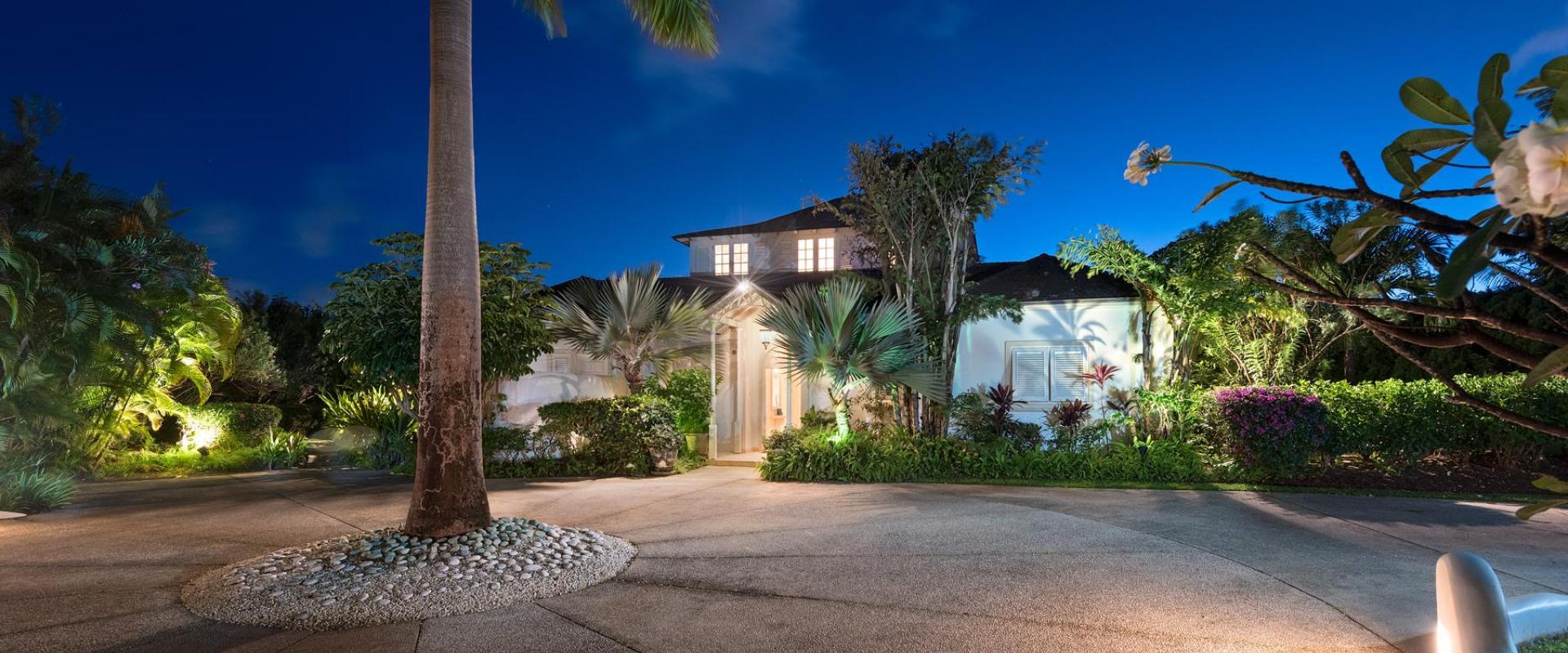 The grand entrance of Villa Rosa at night, warmly lit and surrounded by lush tropical gardens.
