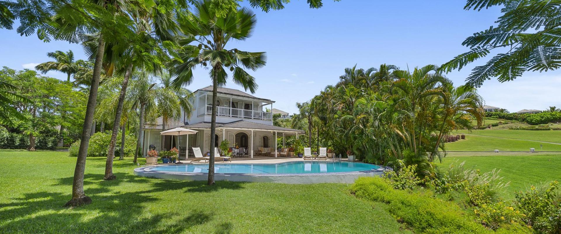 Expansive green gardens with tall palm trees surrounding a private pool at Villa Rosa, Barbados.