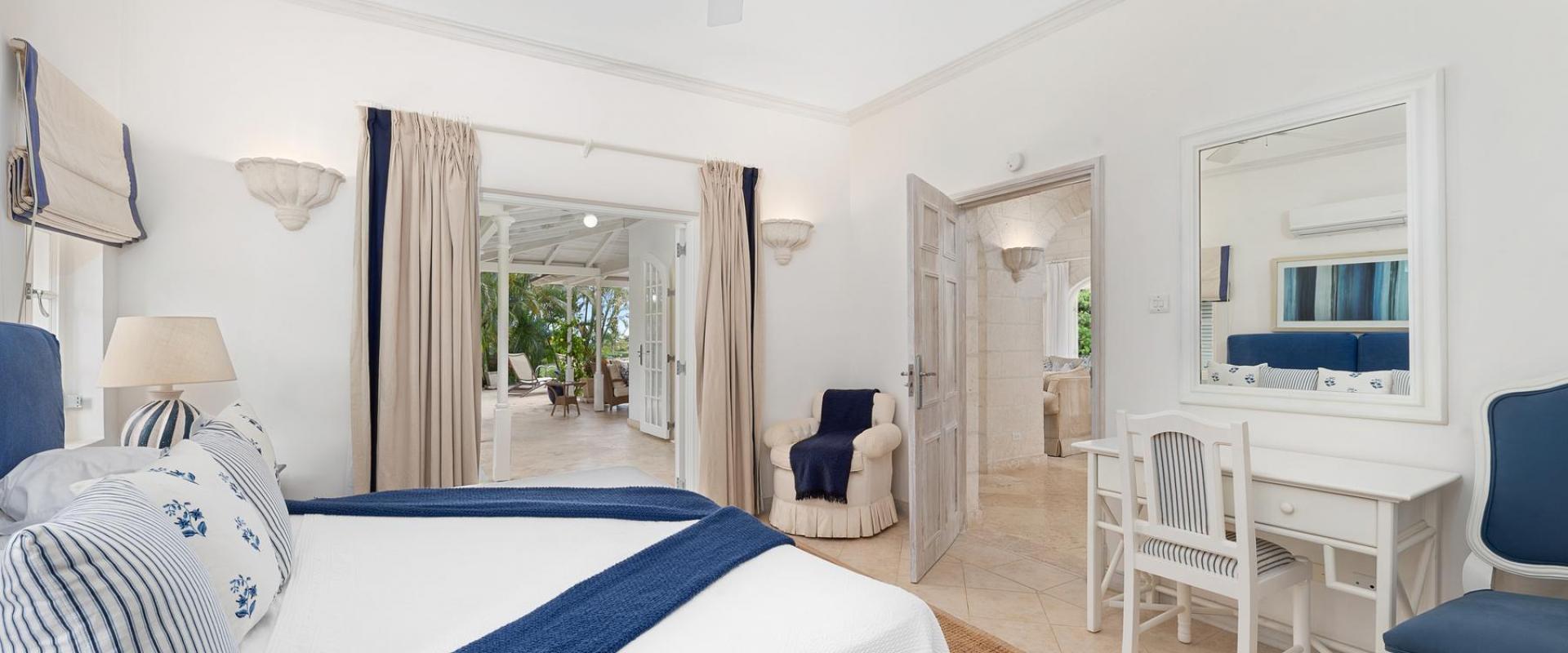 Bright and airy bedroom with a plush blue headboard, direct access to the patio, and garden views at Villa Rosa, Barbados.